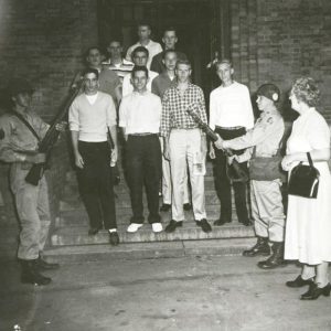 Group of young white men standing on steps with white soldiers and old white woman