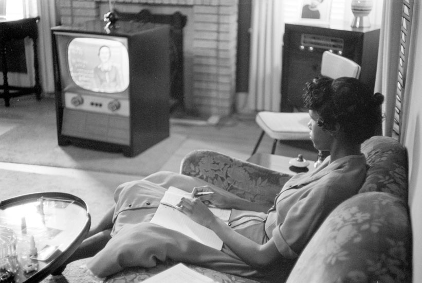 African-American girl taking notes during a television class at home