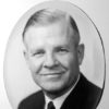 White man smiling in suit and tie in oval frame