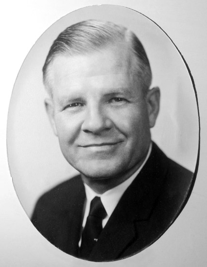 White man smiling in suit and tie in oval frame
