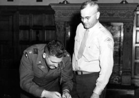 White man in military uniform putting a pin on another white man's uniform jacket