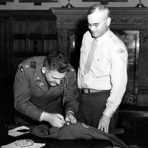 White man in military uniform putting a pin on another white man's uniform jacket