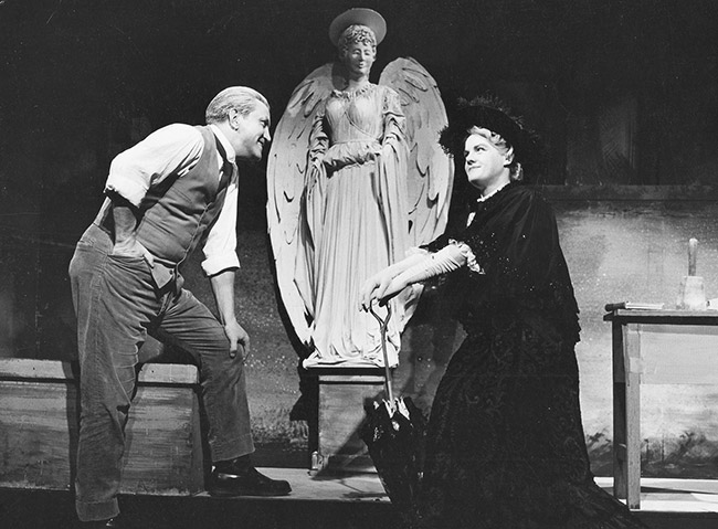 White man and woman in period clothing on stage with angel statue
