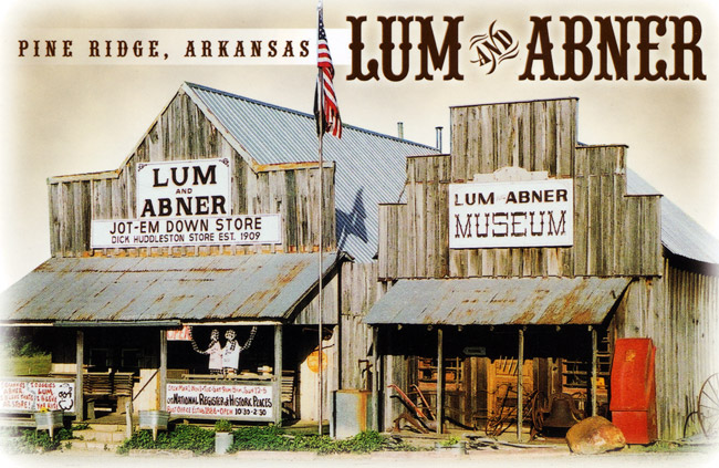 postcard of "Lum and Abner" store and museum fronts with porches signs U.S. flag