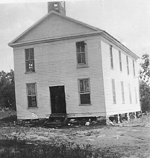 Two-story building with white siding and cupola