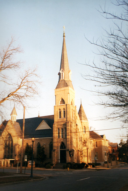 Large brick church with multi story steeple on street corner with bare winter trees