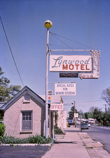 Single-story brick building and hanging "Lynwood Motel" sign on multilane street