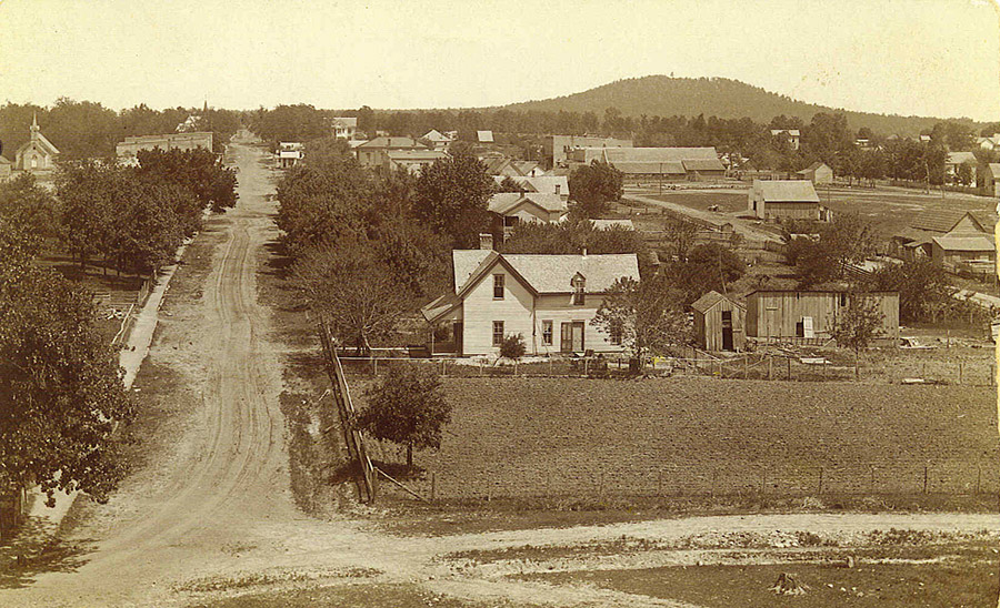 Houses and town buildings on dirt roads with hill in the background