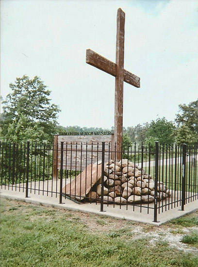 Large cross in pile of rocks with plaque surrounded by iron fence
