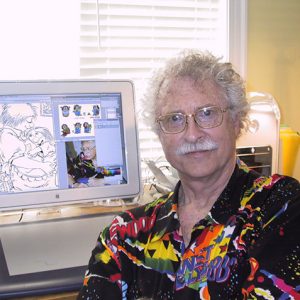 Older white man with glasses and mustache in colorful shirt at computer desk with cartoon images and a photo of himself on the screen