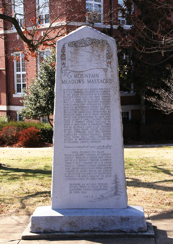 white stone monument with pointed top labeled "The Mountain Meadows Massacre" in front of multistory brick building