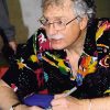 Older white man with glasses and mustache in colorful shirt signing autograph