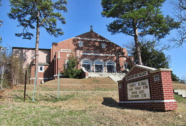 Brick building on hilltop with cross on top stairs and sign