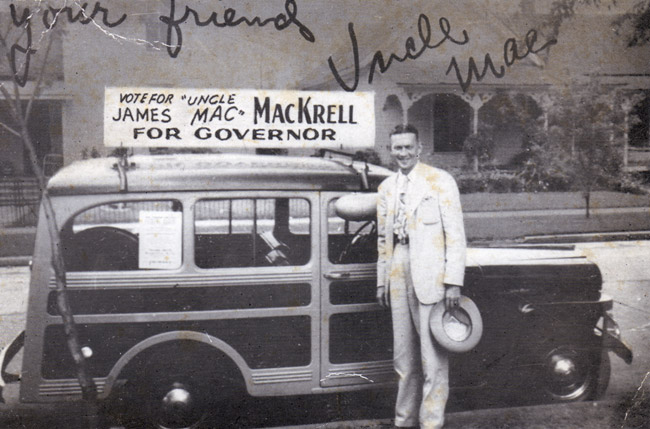 White man in suit with hat posing with a wood paneled car which has a sign on its roof "Vote for James Uncle Mac MacKrell for Governor"
