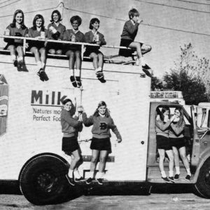 Group of white girls in uniforms posing with milk truck