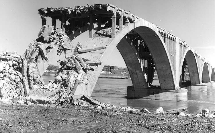 Demolished section of concrete arch bridge over river