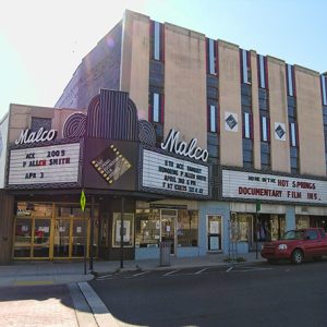Theater building with "Malco" marquee over front doors and street with parked red truck
