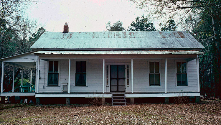 Single-story house with weathered metal roof and covered porch on front and side