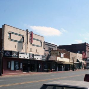 Theater and brick storefronts on street with parked cars on right side