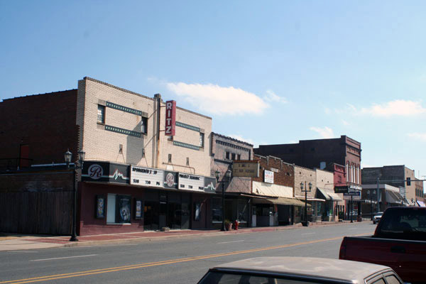 Theater and brick storefronts on street with parked cars on right side
