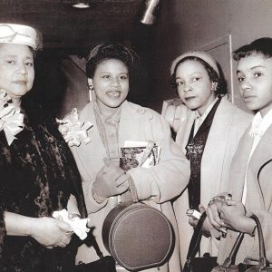 Older African American woman with fur coat and hat standing with two younger and one older African American women in coats