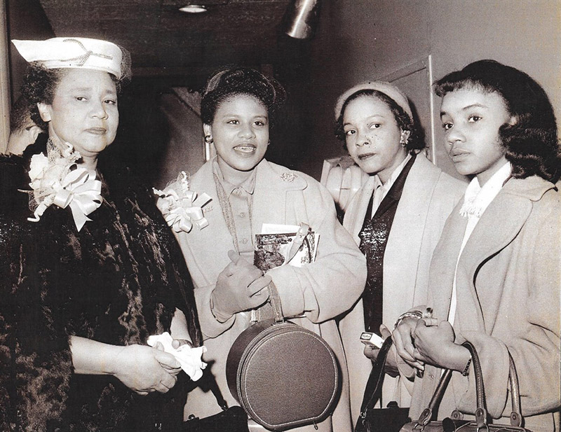 Older African-American woman with hat standing with three younger African-American women in coats