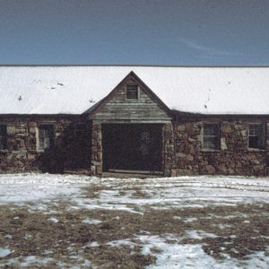Stone building with covered entrance in winter with snow covered roof and grass