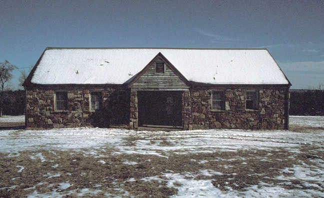 Stone building with covered entrance in winter with snow covered roof and grass