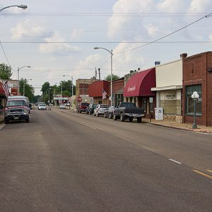Two-lane road with single-story storefronts and parked cars on both sides