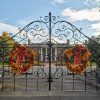 Multicolored autumn wreaths on iron gates with multistory house with covered porch supported by columns behind it