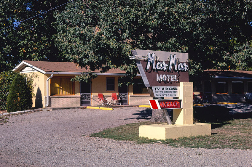 Single-story building behind tree with sign in the foreground