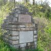 Stone brick monument with "Arkansas" engraved brick and plaque on its base in forested area