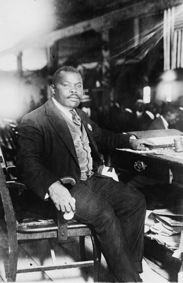 African-American man with mustache in suit vest and tie sitting at desk with book