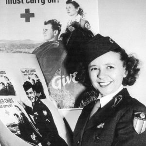 White woman with curly hair in uniform posing with advertisements for the Red Cross