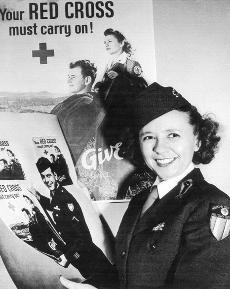 White woman with curly hair in uniform posing with advertisements for the Red Cross