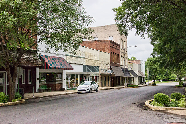 Brick storefronts with trees and parked car on street