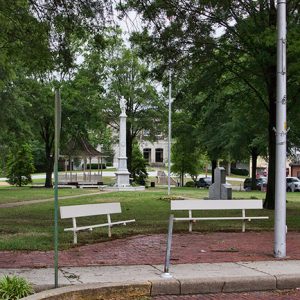 Town park with three benches stone monuments trees flag pole and gazebo