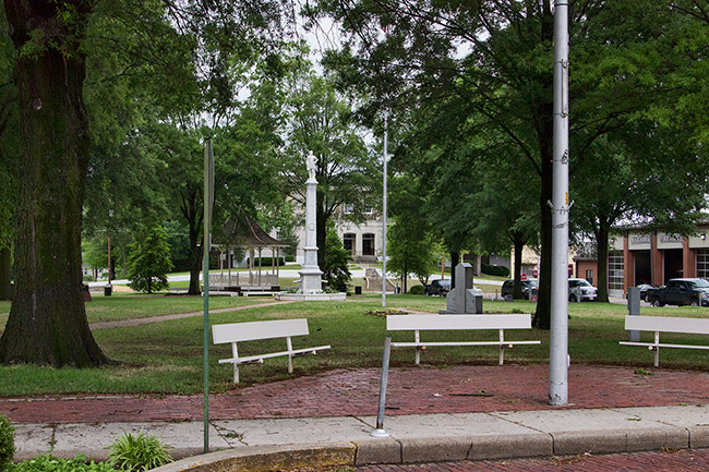 Town park with three benches stone monuments trees flag pole and gazebo