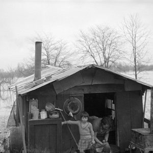 White woman and daughter in makeshift houseboat with stove and smoke stack