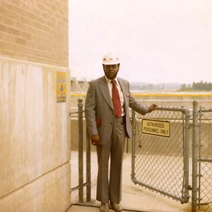 African-American man in suit and hard hat opening gate to parking lot