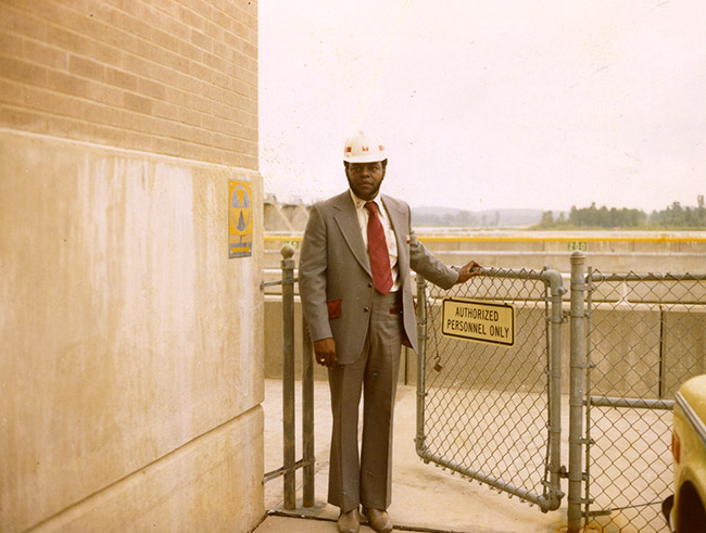African-American man in suit and hard hat opening gate to parking lot