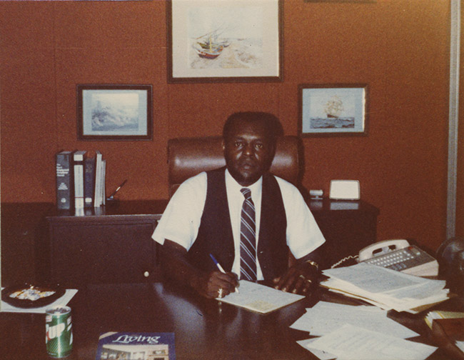 African-American man in shirt vest and tie sitting at his desk