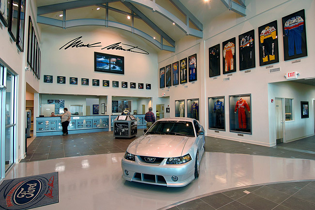 Museum lobby with desk framed uniforms on the walls and silver Ford Mustang car on tiled floor in the foreground