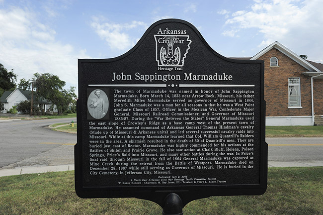 "John Sappington Marmaduke" historical marker sign on street corner with brick building behind it
