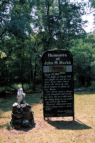 Statue of girl on rock pedestal next to "Homesite of John H. Marks" sign