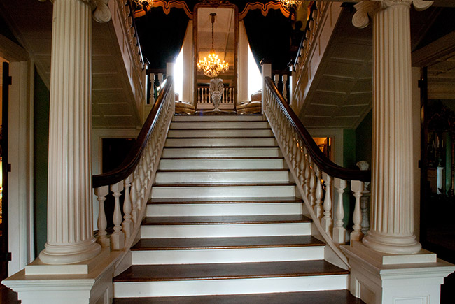 Staircase with railing and columns leading up to mirror with curtains