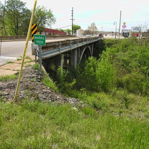 Side view of concrete arch bridge over creek with "Marrs Creek" road sign and railings
