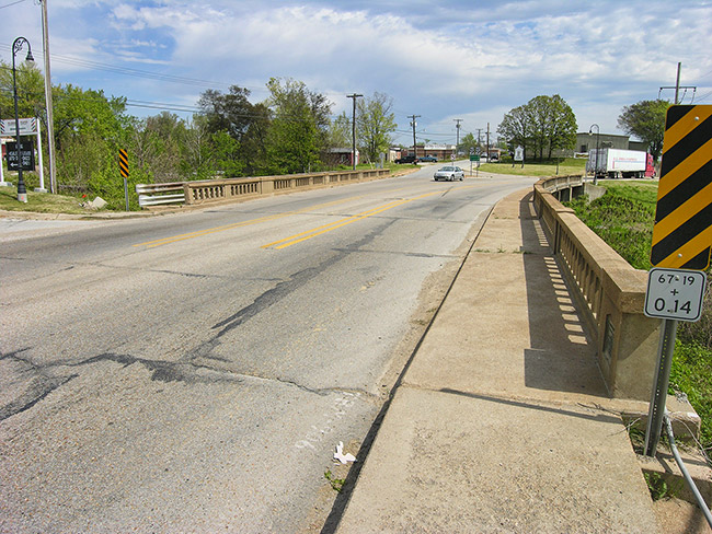 Looking across concrete bridge over creek on two-lane street
