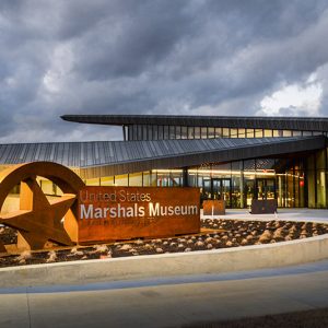 Modern building with badge and "United States Marshals Museum" sign in flower bed in the foreground