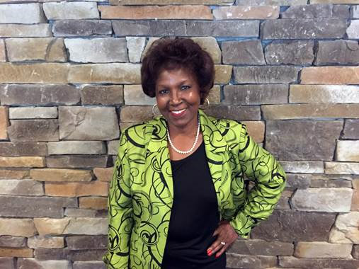 African-American woman smiling in green jacket with stone brick wall behind her
